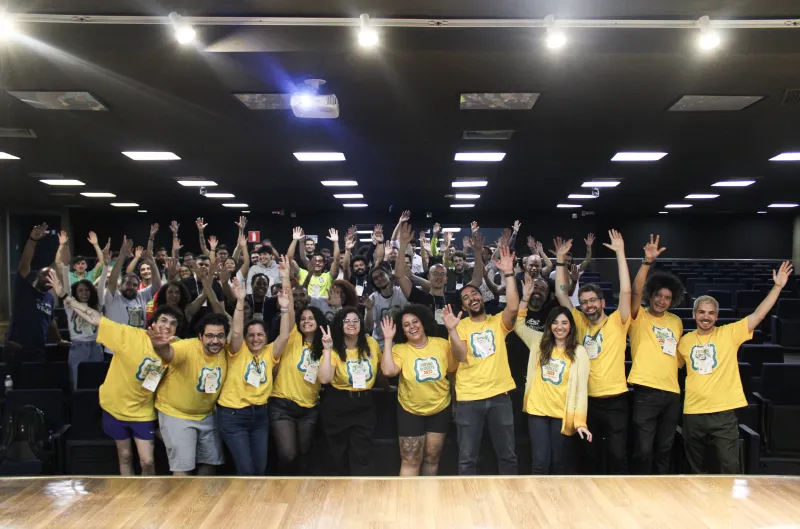 Participantes e organização reunidos no auditório, acenando para a foto.