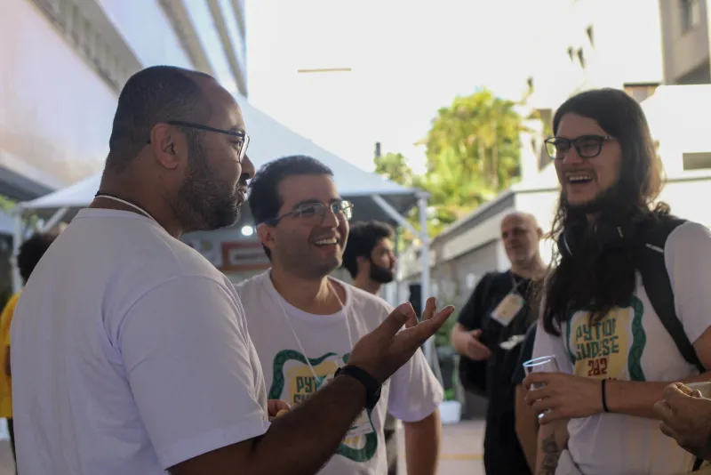 Participantes conversam e sorriem na área externa do evento.