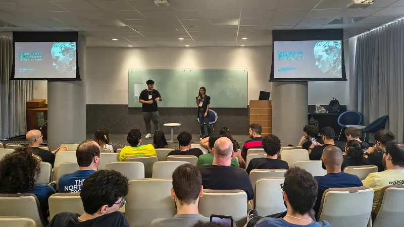 Duas pessoas apresentam uma palestra para o público no auditório.