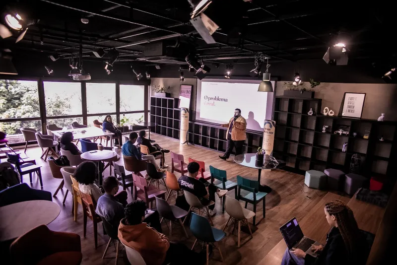 Uma pessoa apresenta uma palestra para participantes sentados no espaço do evento.